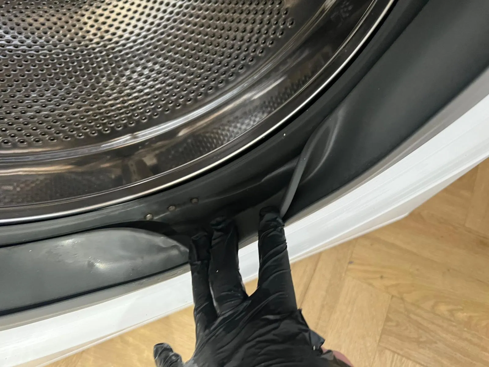 Cleaner in gloves detailing a washing machine door seal